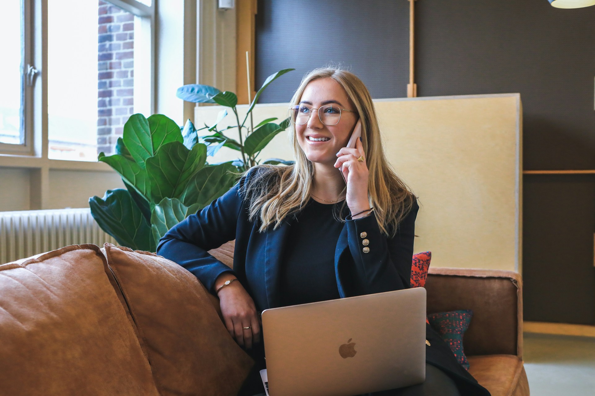 Person smiling at laptop near window with plant, another person standing, "000" text on screen.